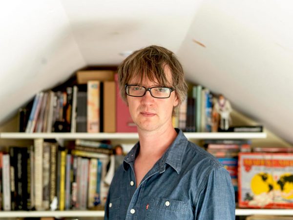 Artist David Blandy looking at the camera in front of shelves of books