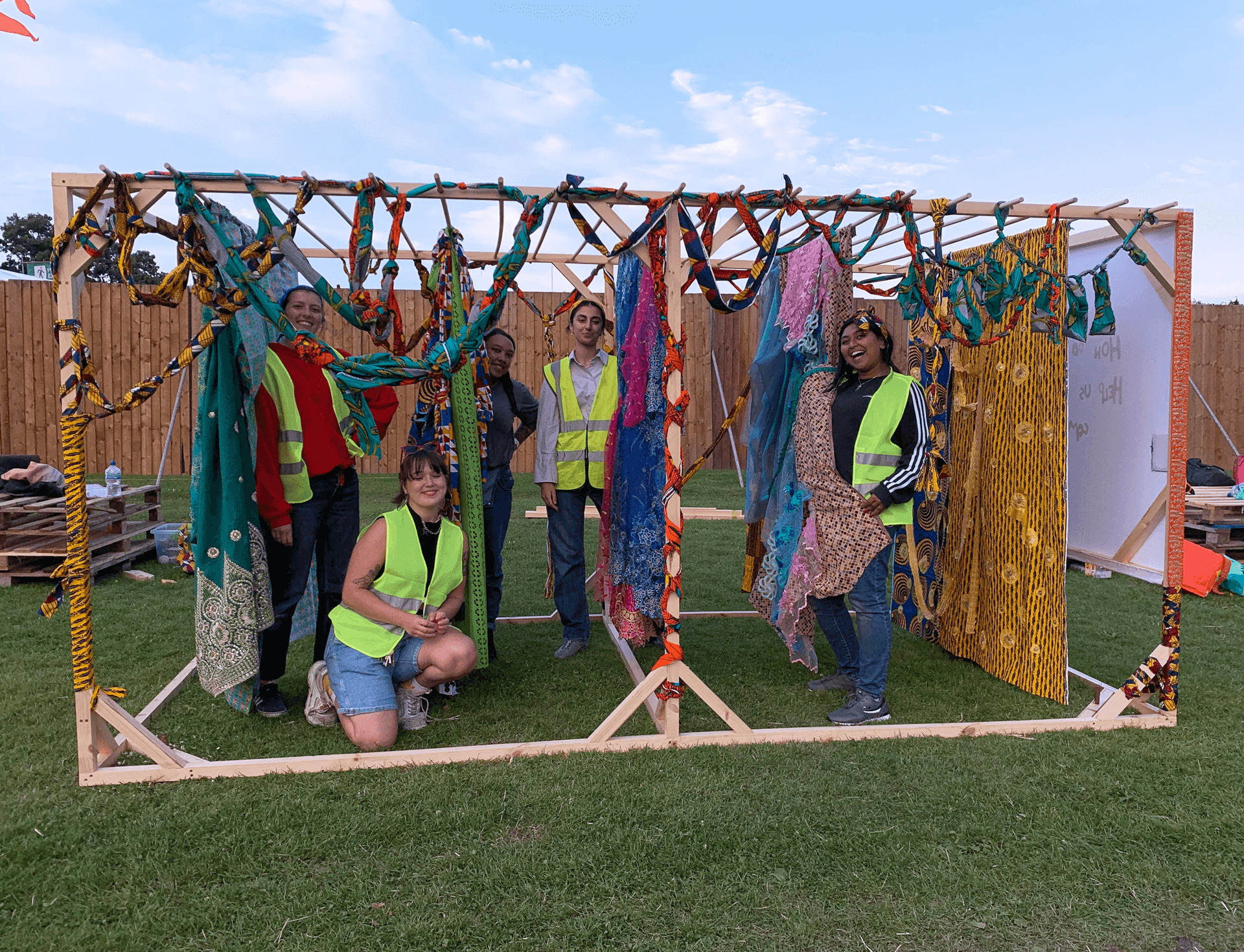 Group of people in hi-vis under a wodden frame with colouful scarves