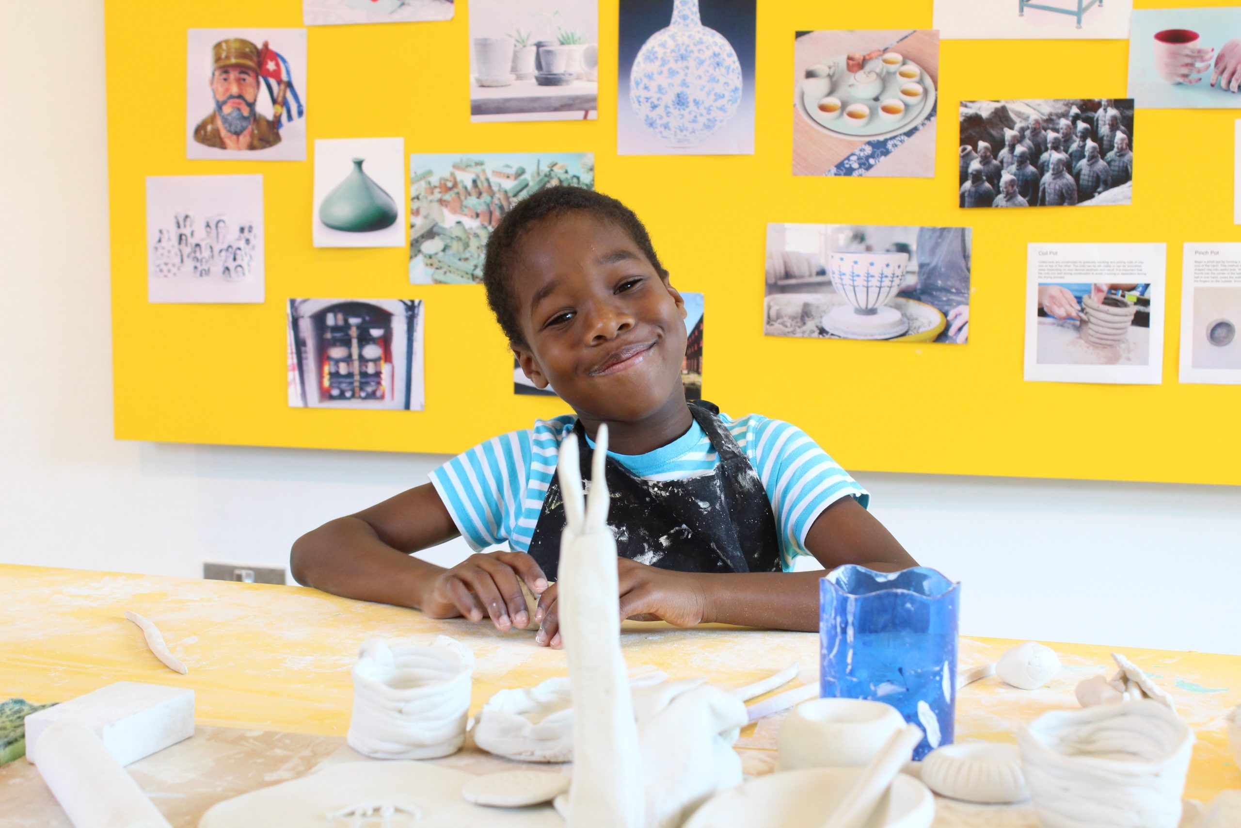 image of a child at Peckham Platform sitting at a table making something out of clay. There is a yellow board behind them with pictures on it.