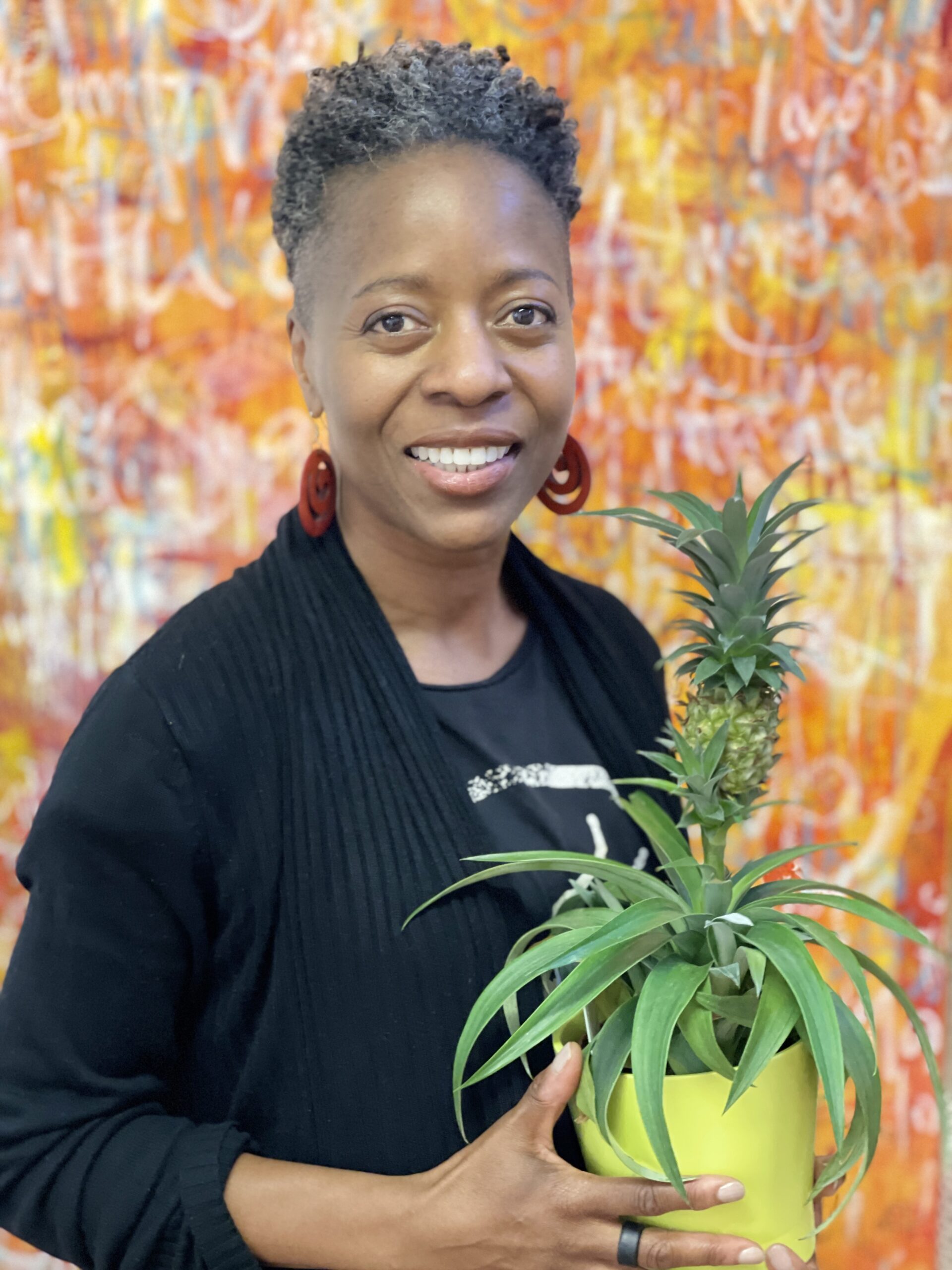 A female with brown skin and short hair smiling holding a green plant